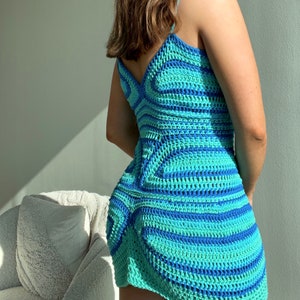 Puede incluir: Un vestido corto de crochet azul y verde con un patr&oacute;n geom&eacute;trico. El vestido tiene un escote en V y tirantes finos.