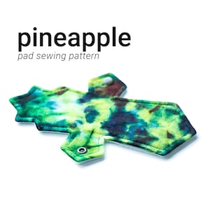 Op de afbeelding: Een groen, blauw en bruin tie-dye menstruatiepad van stof met een witte fleece achterkant. Het pad heeft een drukknoop sluiting en is gelabeld "ananas pad naai patroon".
