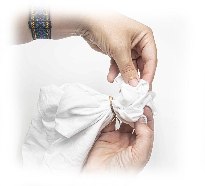 May include: A white cloth is being tied with a rubber band to create a bundle for tie-dyeing.