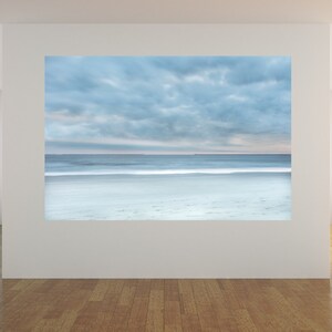 May include: A photograph of a beach scene with a cloudy sky and a calm sea. The sand is white and the water is a light blue colour.