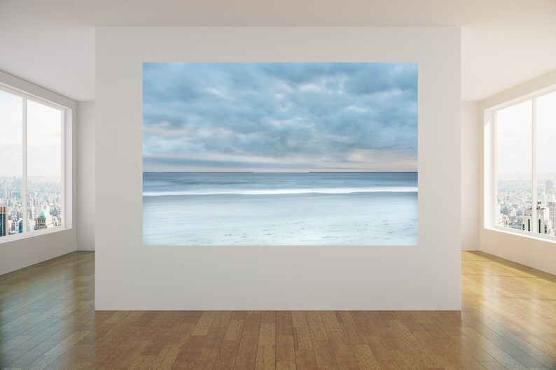 May include: A photograph of a beach scene with a cloudy sky and a calm sea. The sand is white and the water is a light blue colour.