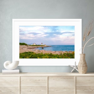 May include: A framed photograph of a white lighthouse on a rocky coast with a blue ocean and a cloudy sky in the background.