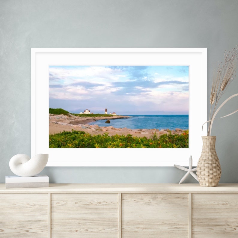May include: A framed photograph of a white lighthouse on a rocky coast with a blue ocean and a cloudy sky in the background.