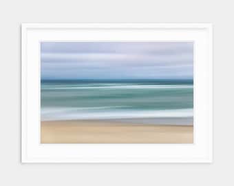 May include: A blurred abstract photograph of a beach scene with a blue sky, blue water, and white waves crashing on the shore. The sand is a light brown color.