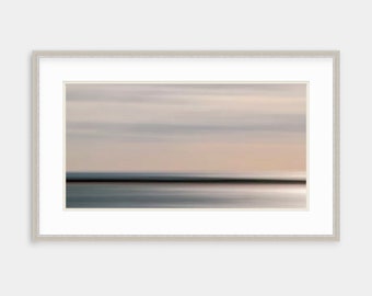 May include: A framed abstract landscape photograph with a blurred background of a sky with clouds and a horizon line of a body of water. The colors are muted and soft, with shades of gray, blue, and pink.