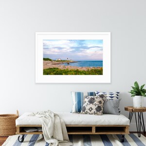 May include: A framed photograph of a lighthouse on a rocky coastline with a blue sky and ocean in the background. The lighthouse is white with a red roof and is located on a small island.