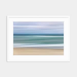 May include: A blurred abstract photograph of a beach scene with a blue sky, blue water, and white waves crashing on the shore. The sand is a light brown color.