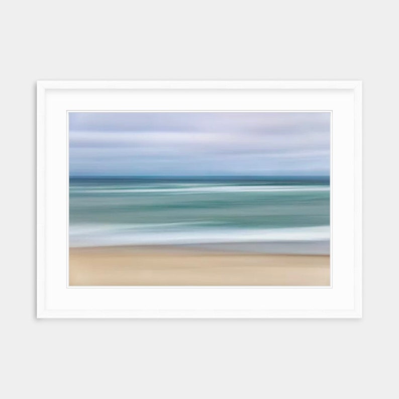 May include: A blurred abstract photograph of a beach scene with a blue sky, blue water, and white waves crashing on the shore. The sand is a light brown color.