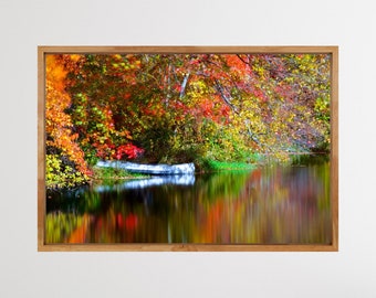 May include: A framed landscape print featuring a serene lake scene. The image captures vibrant autumn foliage in shades of red, orange, and yellow reflected in the calm water. A white canoe rests near the shore, enhancing the tranquil setting.