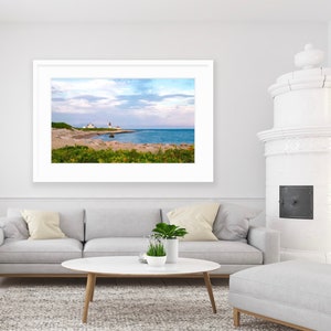 May include: A framed photograph of a lighthouse on a rocky coastline with a blue sky and white clouds. The lighthouse is white with a red roof and is located on a small island.