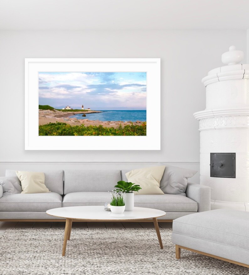 May include: A framed photograph of a lighthouse on a rocky coastline with a blue sky and white clouds. The lighthouse is white with a red roof and is located on a small island.