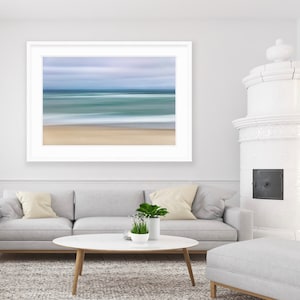 May include: A white framed photograph of a blurred seascape with a light blue sky and a sandy beach.