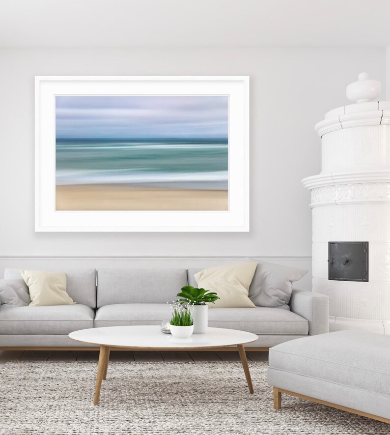 May include: A white framed photograph of a blurred seascape with a light blue sky and a sandy beach.