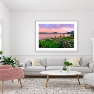 May include: A framed photograph of a lake with a pink and purple sunset sky. The lake is surrounded by green trees and bushes with pink and orange flowers.
