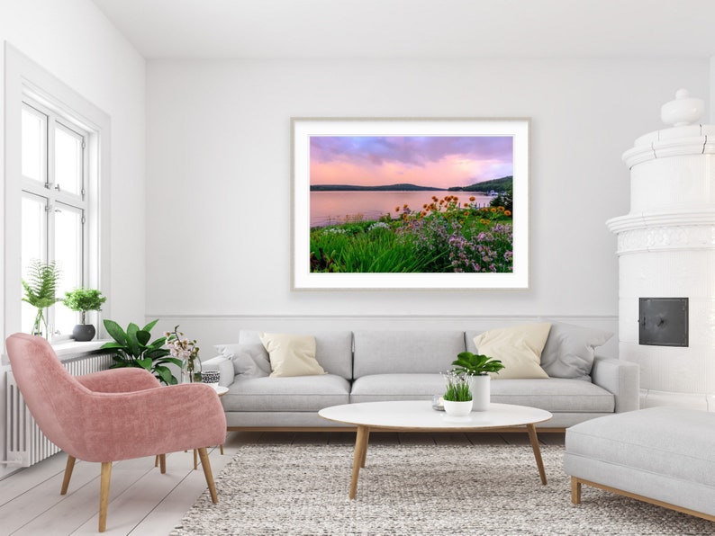 May include: A framed photograph of a lake with a pink and purple sunset sky. The lake is surrounded by green trees and bushes with pink and orange flowers.