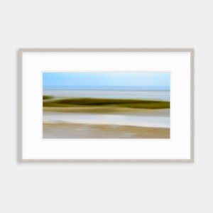 May include: Abstract photograph of a blurred seascape with a green grassy area in the foreground, a white sandy beach, and a blue sky with a horizon line.