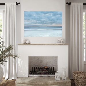May include: A white fireplace with a black metal grate and a wooden mantel. A framed photograph of a cloudy sky and ocean is above the fireplace.