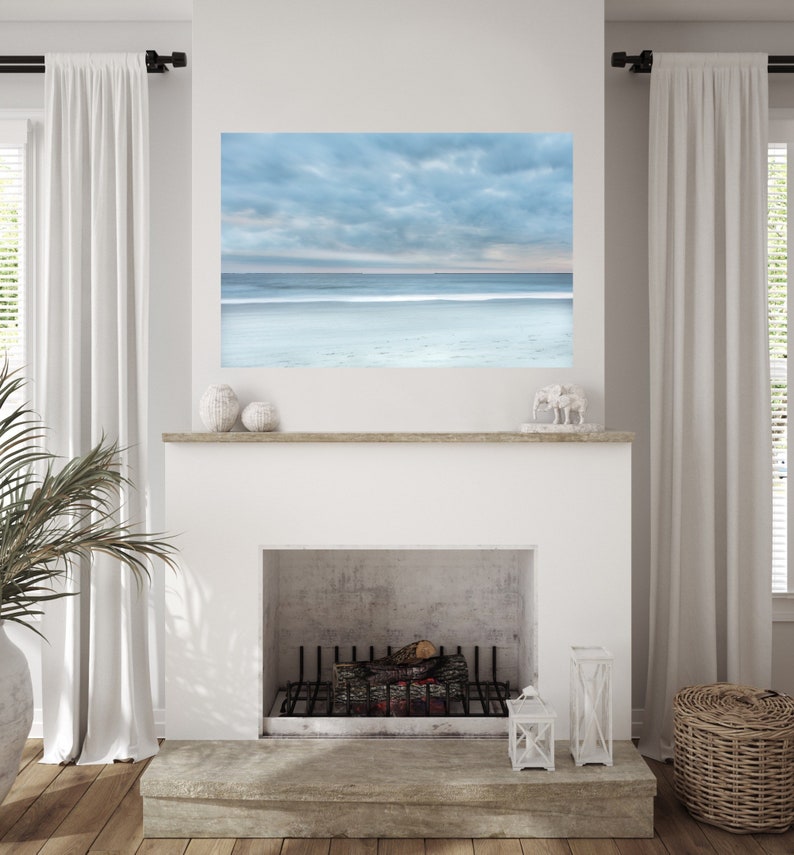 May include: A white fireplace with a black metal grate and a wooden mantel. A framed photograph of a cloudy sky and ocean is above the fireplace.