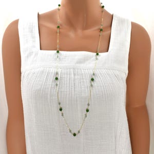 May include: A long gold necklace featuring alternating dark green and light green beads. The necklace is draped around a person's neck, showcasing the delicate chain and the vibrant colors of the beads. The necklace is a piece of jewelry.