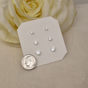 May include: A set of six silver stud earrings with clear cubic zirconia stones. The earrings are displayed on a white card with a silver dime for size comparison.