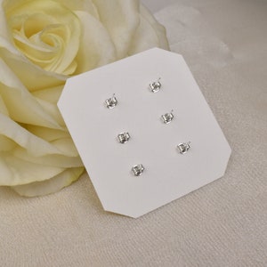 May include: A white card with six silver stud earrings displayed on it. The earrings are arranged in two rows of three. The card is on a white surface.