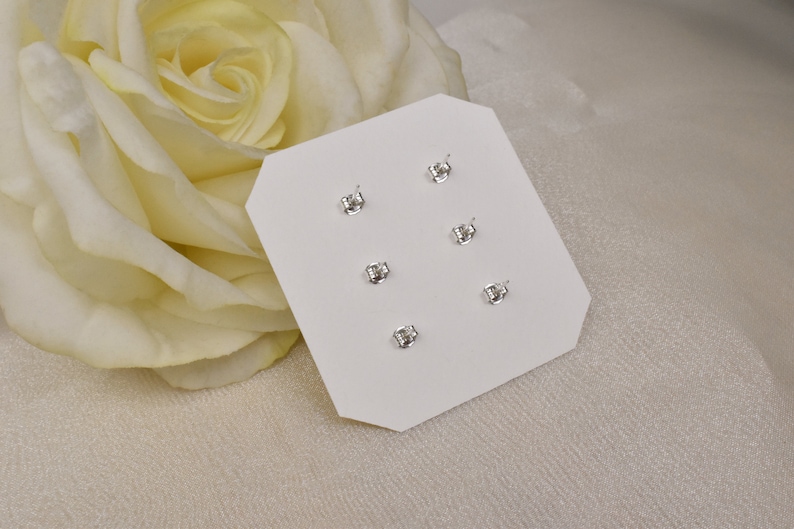 May include: A white card with six silver stud earrings displayed on it. The earrings are arranged in two rows of three. The card is on a white surface.