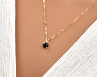 Può includere: Una delicata collana a catena d'oro con un piccolo ciondolo di pietra preziosa nera.