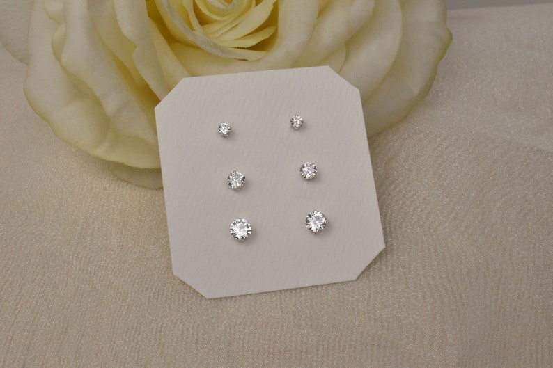 Three pairs of stud earrings of graduated sizes are displayed on a white octagon jewelry card. The round, faceted, twinkling cubic zirconia gems are set in brilliantly shining sterling silver.