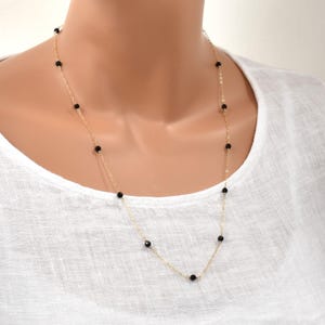 May include: Delicate gold-tone necklace featuring small, evenly spaced black beads. The necklace has a simple, elegant design, perfect for layering or wearing alone. The beads are a deep black color, contrasting with the gold chain.