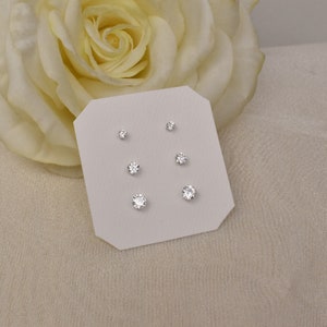 May include: A set of three pairs of silver stud earrings with clear round cubic zirconia stones. The earrings are displayed on a white card.