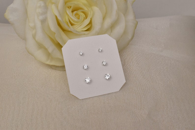 May include: A set of three pairs of silver stud earrings with clear round cubic zirconia stones. The earrings are displayed on a white card.