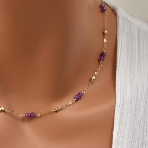 May include: A fine gold necklace adorned with small, round, purple gemstones and gold beads. The necklace is set against a white backdrop, accentuating the contrast between the gold and purple.