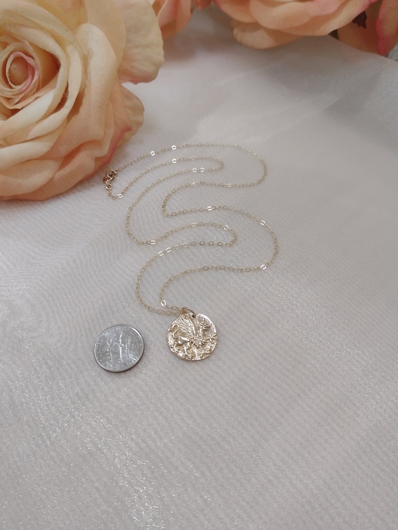 The griffin pendant is placed next to a dime. They are very similar in size, the pendant being slightly larger than the dime. The chain and pendant are of the same gold color, and look very shiny.
