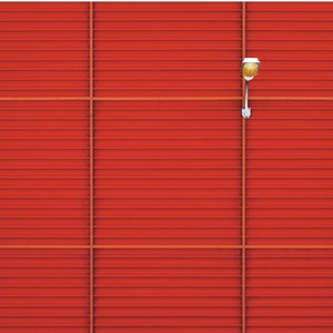 Puede incluir: Una pared de metal corrugado roja con una sola luminaria montada en el lateral. La pared está dividida en secciones por líneas horizontales. La pared está delante de un suelo nevado.