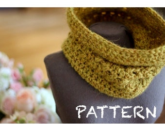 May include: A crocheted cowl in a muted green color, displayed on a mannequin. The cowl is folded over and has a textured stitch pattern. The word "PATTERN" is written in white chalk on the mannequin's chest.