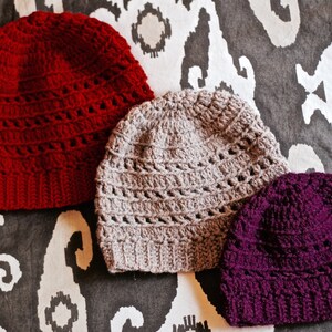 May include: Three crocheted hats in different colors: red, gray, and purple. The hats are made with a lacy stitch pattern.