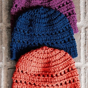 May include: Three crocheted hats stacked on top of each other. The top hat is purple, the middle hat is blue, and the bottom hat is orange.