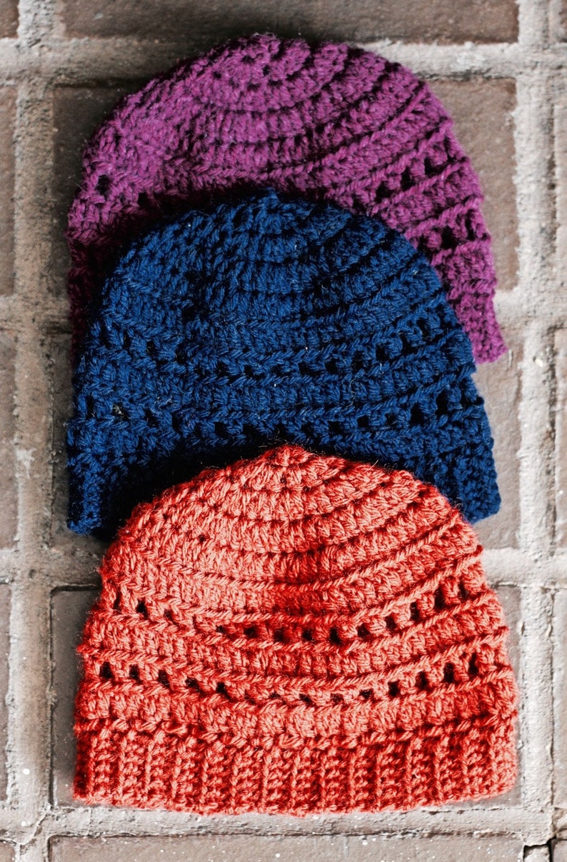 May include: Three crocheted hats stacked on top of each other. The top hat is purple, the middle hat is blue, and the bottom hat is orange.