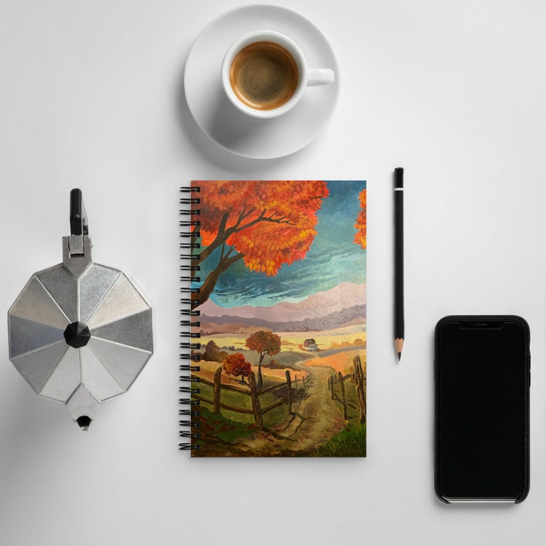 May include: A spiral bound notebook with a colorful painting of a fall landscape. The painting features a large tree with orange and red leaves, a winding path, and a small house in the distance.