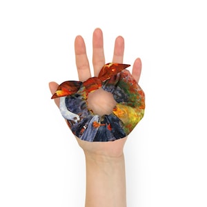 May include: A colorful hair scrunchie with a painting of a group of people in a field. The scrunchie is made of fabric and has a bow on top.