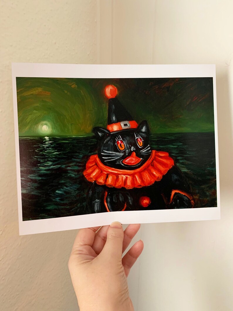 Op de afbeelding: Een zwarte kat met een rode en oranje narrenmuts en kostuum, met een rode neus en grote ogen, drijft in een donkergroene zee met een heldere maan op de achtergrond.