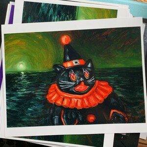 Op de afbeelding: Een zwarte kat met een rood-oranje narrenmuts en een rood-oranje kraag staat tegen een donkergroene en blauwe achtergrond. De kat heeft felrode ogen en een roze neus.