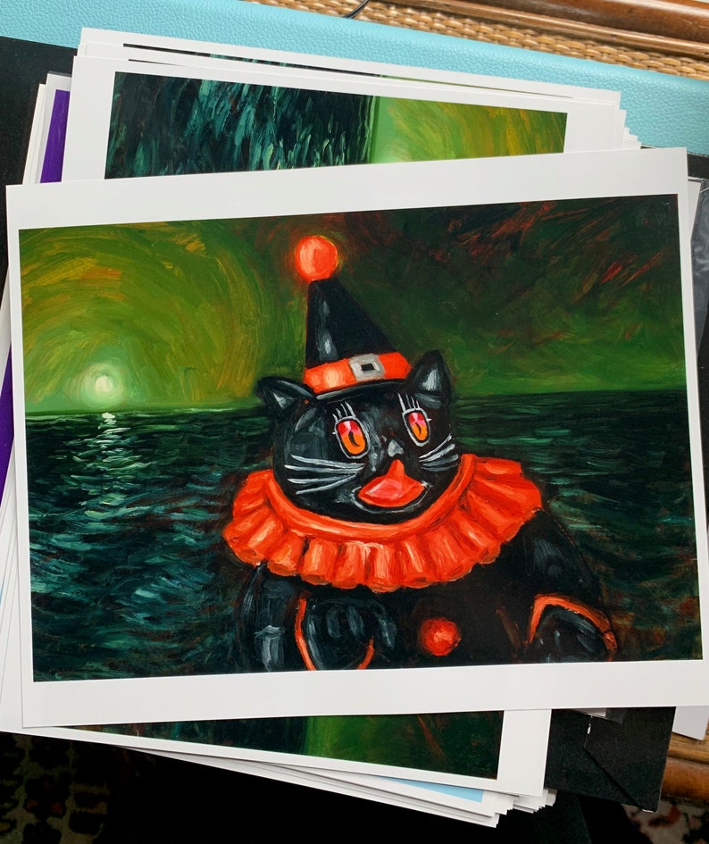 Op de afbeelding: Een zwarte kat met een rood-oranje narrenmuts en een rood-oranje kraag staat tegen een donkergroene en blauwe achtergrond. De kat heeft felrode ogen en een roze neus.