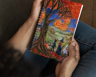 May include: A spiral bound notebook with a colorful illustration of a witch, a black cat, and a ghost trick-or-treating under a tree with jack-o-lanterns hanging from the branches. The background is a fall scene with orange, red, and yellow leaves.