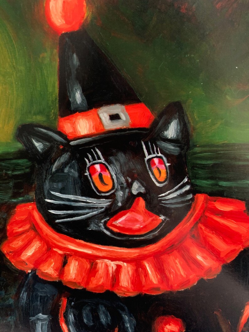 Op de afbeelding: Een zwarte kat met een rood-zwarte hoed en een rode geruite kraag. De kat heeft een rode neus en grote, oranje ogen. De achtergrond is groen.