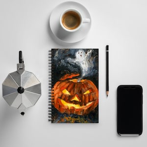 Puede incluir: Una libreta de espiral con fondo negro y una pintura de una calabaza de Halloween con un fantasma volando desde la parte superior. La calabaza es naranja y tiene una cara de miedo.