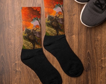 May include: A pair of black socks with a colorful autumn scene featuring a witch riding a horse and holding a jack-o-lantern. The scene is set against a backdrop of orange, yellow, and red leaves.