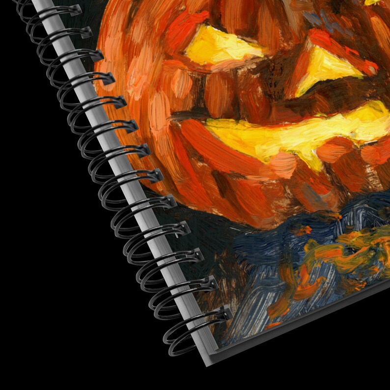 Puede incluir: Un cuaderno de espiral con una imagen pintada de una calabaza de Halloween en la portada. La calabaza es naranja y amarilla con una cara de miedo.