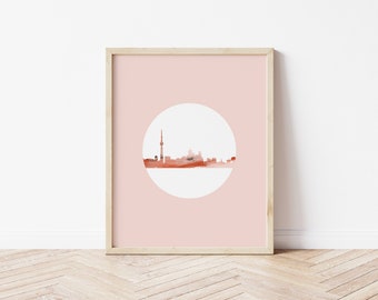 May include: A framed print with a pink background and a white circle in the center. The circle contains a silhouette of the Toronto skyline in shades of orange and brown.