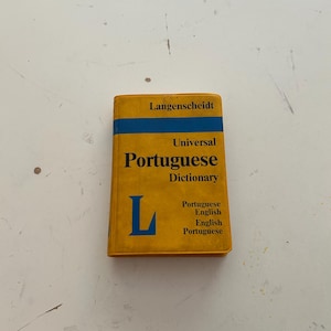 May include: A yellow and blue Langenscheidt Universal Portuguese-English Dictionary. The book has the word "Portuguese" in large letters. The cover also has the word "Dictionary" and the letter "L" in blue.